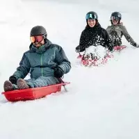 Groupe d’adultes descendant en luge sur une piste enneigée avec éclaboussures de neige aux Arcs 1800
