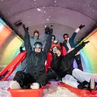 Groupe d’adultes en luge dans un tunnel coloré avec lumières arc-en-ciel aux Arcs 1800