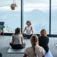 Groupe de personnes pratiquant le yoga assis devant de grandes baies vitrées avec vue sur les montagnes