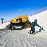 Deux snowboardeurs s'apprêtent à passer sous la structure en bois monumentale marquant l'entrée du S Park aux Arcs, sur un domaine skiable parfaitement damé