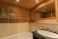 Salle de bain avec baignoire, vasque et habillage en bois dans un appartement aux Arcs