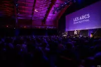 Public réuni devant la scène et le grand écran des Arcs Film Festival 2025, dans une salle éclairée de violet.