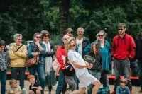 Groupe de personnes souriantes et enthousiastes, certaines portant des lunettes de soleil et des vêtements décontractés, observant un joueur de tennis en action.