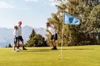 Jeunes golfeurs sur le parcours du golf des Arcs avec les sommets alpins en arrière-plan.