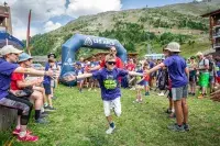 Enfant courant sous un tunnel formé par les bénévoles lors du Hero Game aux Arcs, événement estival en montagne.