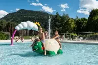 Enfants s’amusant dans la piscine extérieure de Bourg Saint Maurice avec jeux d’eau et vue sur la montagne.