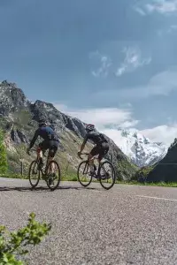 Deux cyclistes gravissent une route de montagne avec glaciers en arrière-plan.
