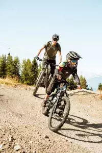 Famille de cyclistes en VTT sur un chemin de montagne, entourée de forêt.