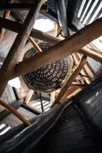 Intérieur d'une cabane géante montrant l'assemblage de poutres en bois brut et un filet de repos en forme de nid suspendu.