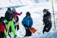 Enfants apprenant les gestes de secours en avalanche avec une pisteuse.