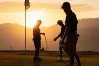 Joueurs de golf sur un green au coucher du soleil en montagne.