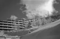 Immeuble de montagne installé sur un versant enneigé sous un ciel nuageux.