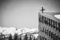 Skieur debout sur le toit d’un bâtiment avec les montagnes enneigées en arrière-plan.