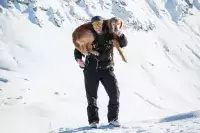Pisteuse portant un chien de secours dans un décor alpin enneigé.