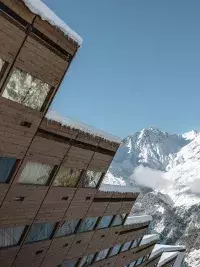 Een typisch houten gebouw uit Les Arcs met uitzicht op besneeuwde bergtoppen onder een blauwe hemel