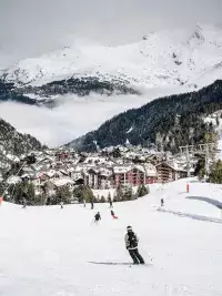 Vue panoramique du village des Arcs enneigé avec les pistes et les sommets alpins en arrière-plan.