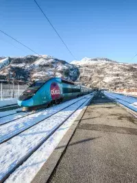 Train OUIGO à quai dans une gare alpine entourée de montagnes enneigées.
