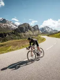 Cycliste en tenue sportive roulant sur une route de montagne au cœur des paysages alpins