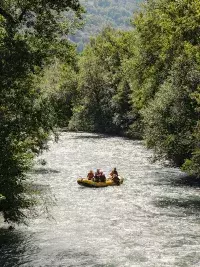 Bateau de rafting avec plusieurs personnes naviguant sur une rivière bordée d’arbres en été