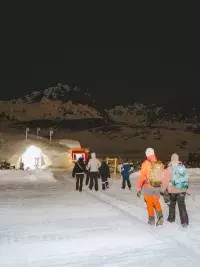 Groupe de personnes marchant vers un igloo éclairé de nuit dans un paysage enneigé aux Arcs