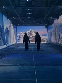 Deux personnes marchant dans un tunnel immersif avec projections de sommets enneigés et paysages de montagne à l’Aiguille Rouge