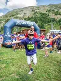 Enfant courant sous un tunnel formé par les bénévoles lors du Hero Game aux Arcs, événement estival en montagne.