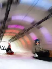 Personnes descendant en luge dans un tunnel éclairé avec lumières colorées aux Arcs 1800