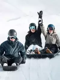 Trois personnes en luge descendant une piste enneigée et s’amusant aux Arcs 1800