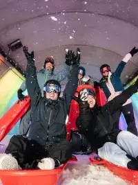 Groupe d’adultes en luge dans un tunnel coloré avec lumières arc-en-ciel aux Arcs 1800