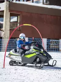 Enfant conduisant une mini-motoneige sur la neige dans une station de ski avec parcours sécurisé