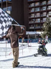 Enfant franchissant la ligne d’arrivée en mini-motoneige avec drapeau à damier dans une station de ski