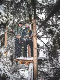 Deux participants attachés à une ligne de vie sur une plateforme d’accrobranche au milieu des sapins enneigés