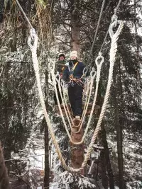 Deux personnes évoluant sur un parcours accrobranche enneigé en forêt, équipées de harnais