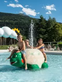 Enfants s’amusant dans la piscine extérieure de Bourg Saint Maurice avec jeux d’eau et vue sur la montagne.