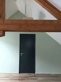 Mur peint sous charpente apparente avec porte noire