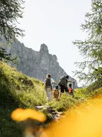 Famille marchant sur un sentier de montagne avec sacs à dos et bâtons de randonnée
