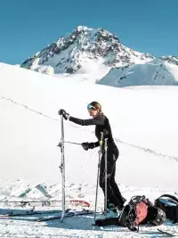 Femme en ski de randonnée préparant son équipement avec skis et bâtons face à un paysage de montagne enneigé aux Arcs