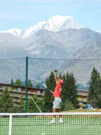 Joueur de tennis servant sur un court avec vue sur les montagnes et le Mont Blanc en arrière-plan