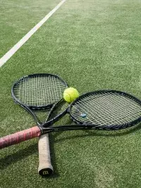 Deux raquettes de tennis croisées avec une balle posées sur un court en gazon synthétique