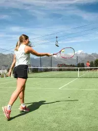 Joueuse de tennis frappant la balle sur un court extérieur avec vue sur les montagnes et télésièges