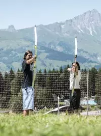 Deux personnes pratiquant le tir à l’arc en extérieur avec un paysage de montagne en arrière-plan