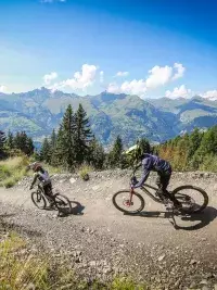 Trois vététistes descendant un sentier de montagne avec vue sur les sommets alpins