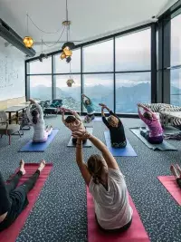 Groupe en séance de yoga étirant les bras dans une salle avec grandes fenêtres ouvertes sur les sommets