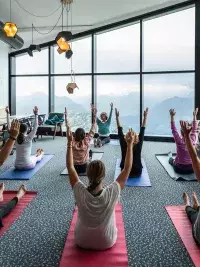 Participants levant les bras en yoga assis dans un espace intérieur avec vue sur un paysage alpin