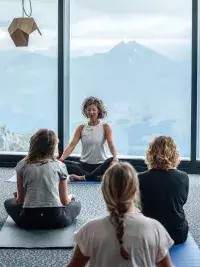 Groupe de personnes pratiquant le yoga assis devant de grandes baies vitrées avec vue sur les montagnes