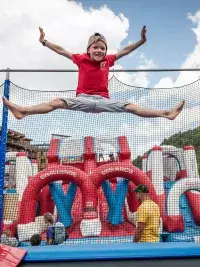 Un garçon réalise un saut en extension sur un trampoline sécurisé par des filets, lors d'une journée d'activités estivales aux Arcs