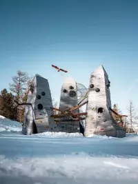 Intérieur d'une cabane géante montrant l'assemblage de poutres en bois brut et un filet de repos en forme de nid suspendu