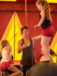 Des enfants s'initient à l'équilibre sur un ballon sous un chapiteau de cirque aux Arcs, encadrés par une animatrice
