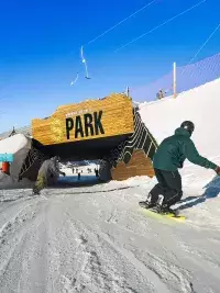 Deux snowboardeurs s'apprêtent à passer sous la structure en bois monumentale marquant l'entrée du S Park aux Arcs, sur un domaine skiable parfaitement damé