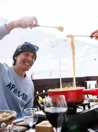 Personnes partageant une fondue en terrasse face aux montagnes enneigées